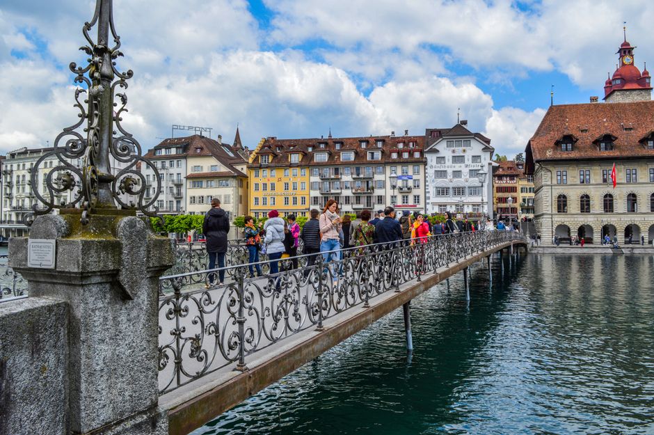 People walking on aged pedestrian bridge with decorative elements crossing river channel and leading to old town in daytime