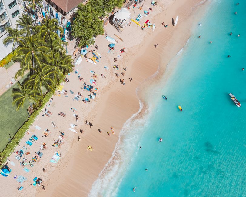 Aerial view capturing people enjoying a sunny day at the beach with turquoise waters and vibrant surroundings.