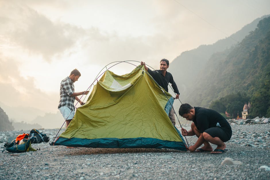 Men setting up a tent on a rocky mountain landscape under a cloudy sky, showcasing outdoor adventure.