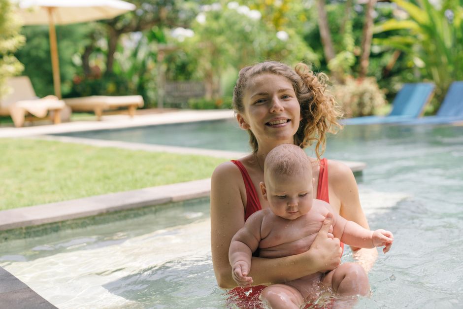 A smiling mother and her baby enjoying a sunny day in an outdoor pool, embracing togetherness.