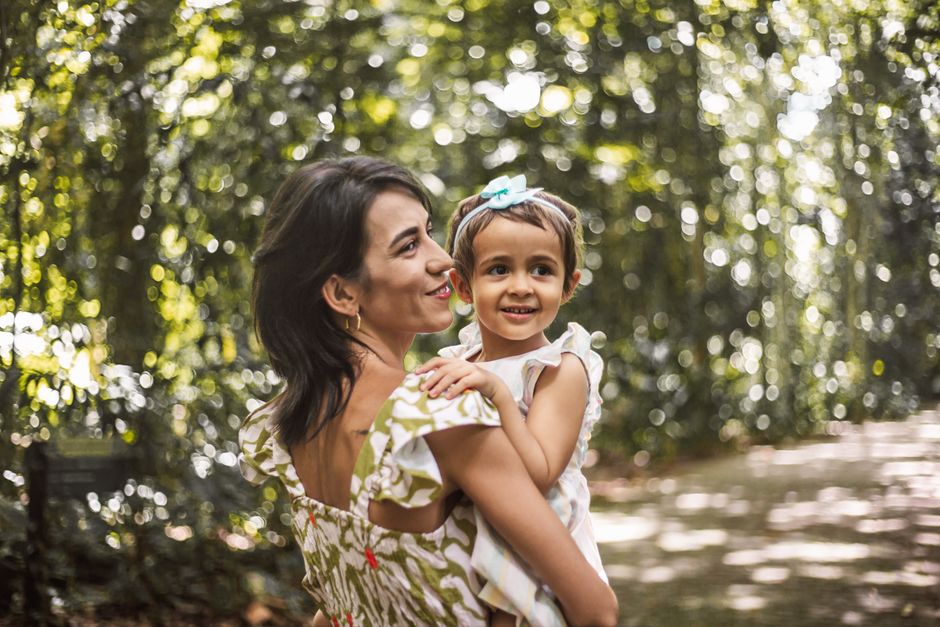 A cheerful mother and daughter embracing in a lush green park, enjoying a sunny day together.
