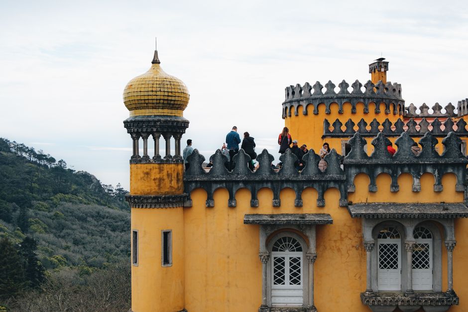 Colorful yellow towers of Pena Palace in Sintra, Portugal with visitors exploring its historic architecture.