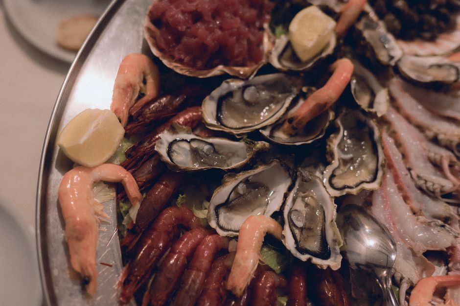 A seafood platter featuring oysters, shrimp, and tuna with lemon garnish.