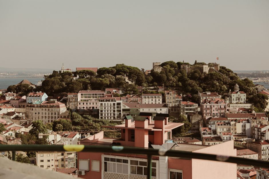 A picturesque panorama of Lisbon cityscape highlighting Saint George's Castle with lush greenery on a hilltop.