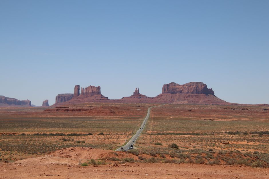 Iconic Monument Valley with a long road stretching through a vast desert landscape on a clear day.