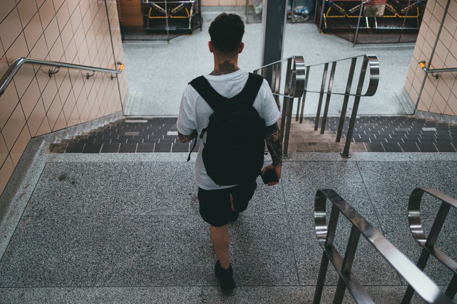Back view of a man with tattoos walking down subway stairs in a city environment.