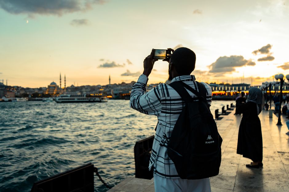 Tourists taking photos of a scenic sunset along the Bosphorus in Istanbul with historical mosques in the background.