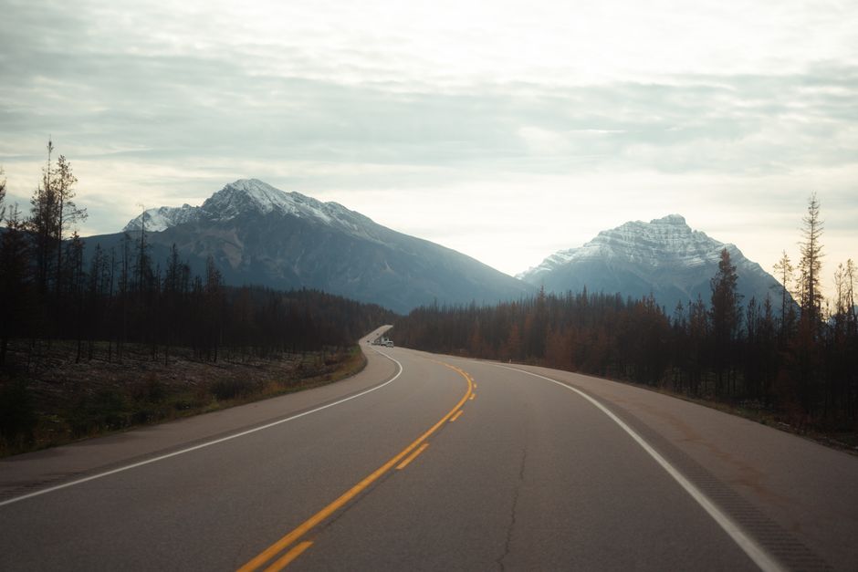 A peaceful highway winding through a mountainous landscape under a cloudy sky.