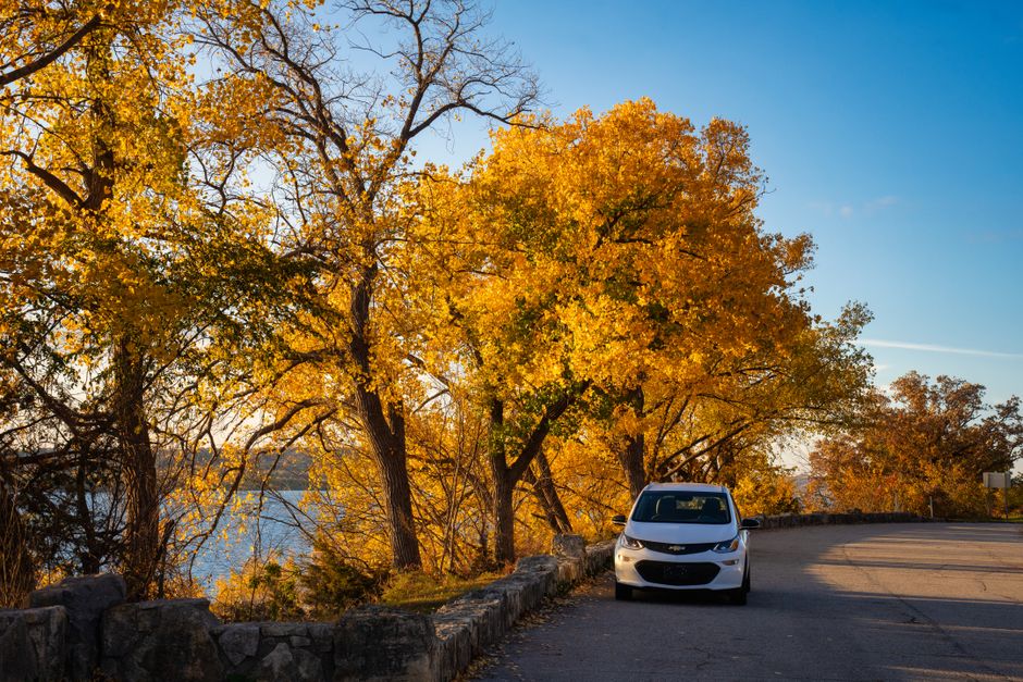 A car parked along a vibrant autumn road with golden trees and blue sky in Stockholm, WI.