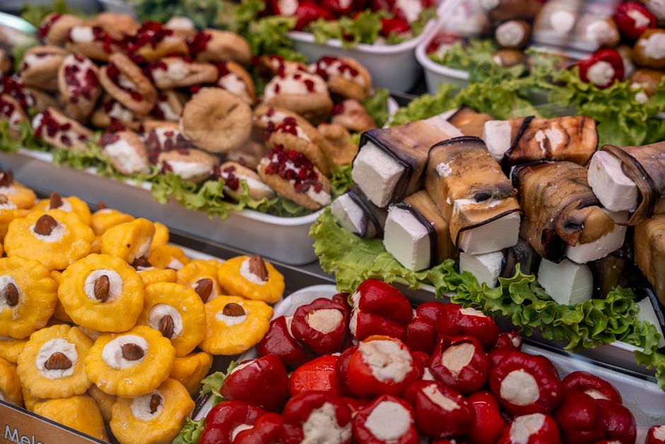Colorful display of gourmet stuffed vegetables and cheese rolls on leafy beds.