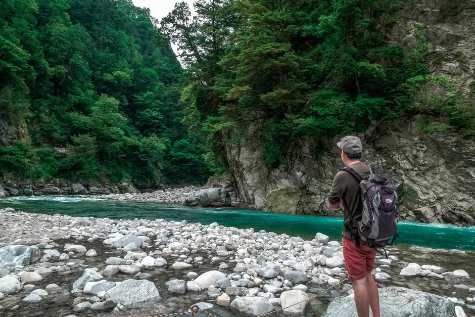 Explore nature's tranquility with a solo traveler by vibrant turquoise river and lush green forest.
