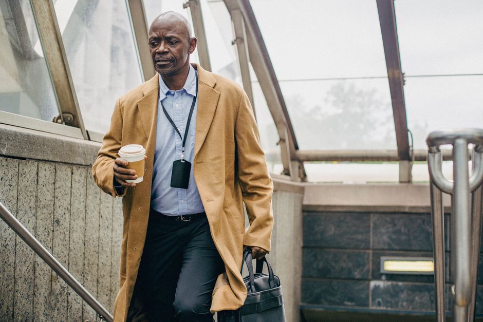 Pensive middle aged ethnic male office worker with takeaway coffee walking on staircase while looking down in building