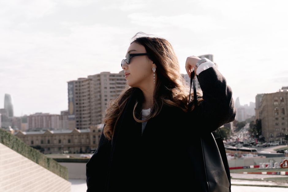 Stylish woman wearing sunglasses and coat in urban setting, showcasing modern elegance.