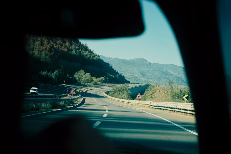 A scenic view of a winding highway passing through lush mountains, captured from inside a vehicle.