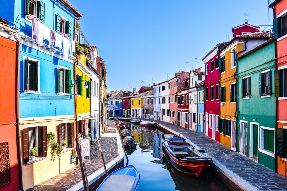 Vibrant and colorful houses line a canal in Burano, Venice, Italy, showcasing unique architecture and charm.