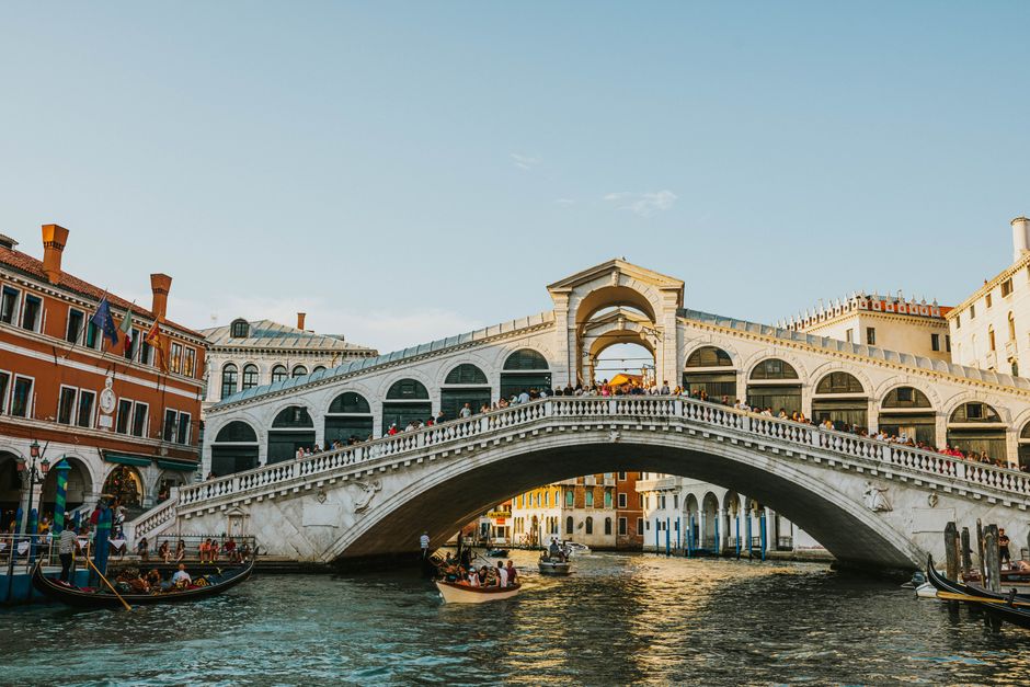 The iconic Rialto Bridge spanning the Grand Canal in Venice, bathed in daylight, with gondolas passing beneath.