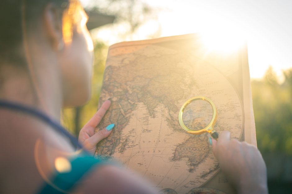 A person examines a world map using a magnifying glass outdoors in bright sunlight, capturing a sense of exploration.