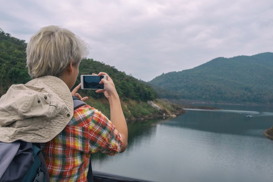 Person photographing a beautiful mountain lake view with a smartphone, enjoying outdoor adventure.