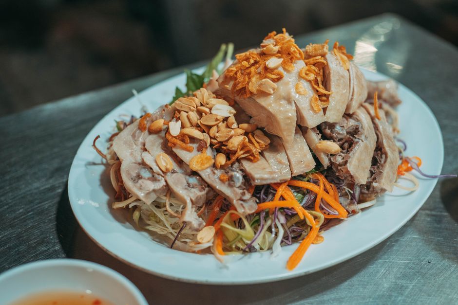 Plate of Vietnamese salad with chicken, carrots, and peanuts served indoors on a metal table.