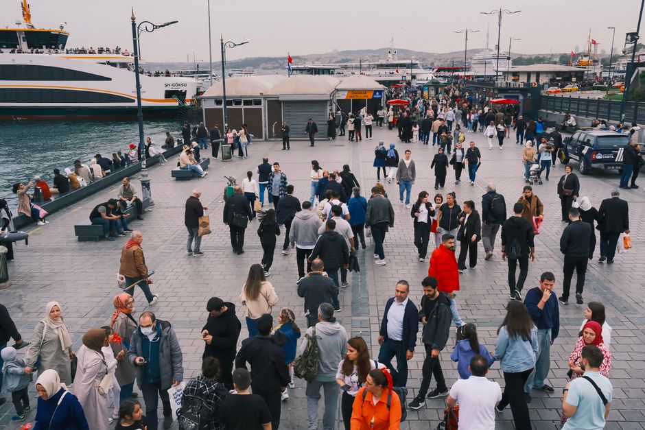 A bustling promenade at Istanbul harbor filled with people walking and a ship docked nearby.