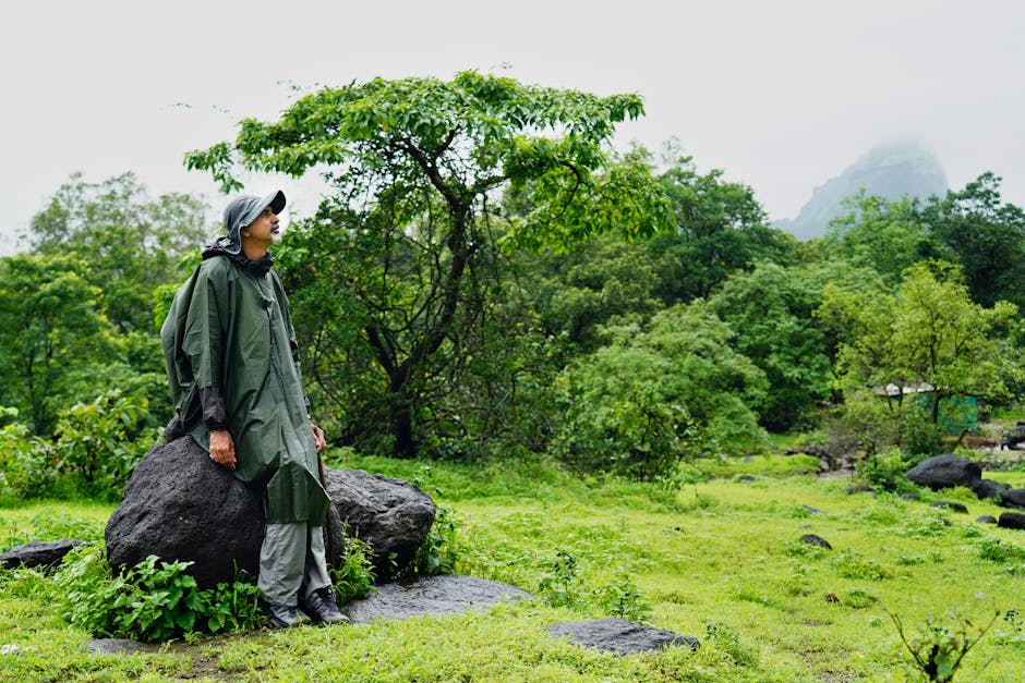 A man in a raincoat stands amidst lush greenery in Lonavala, India, showcasing natural beauty.